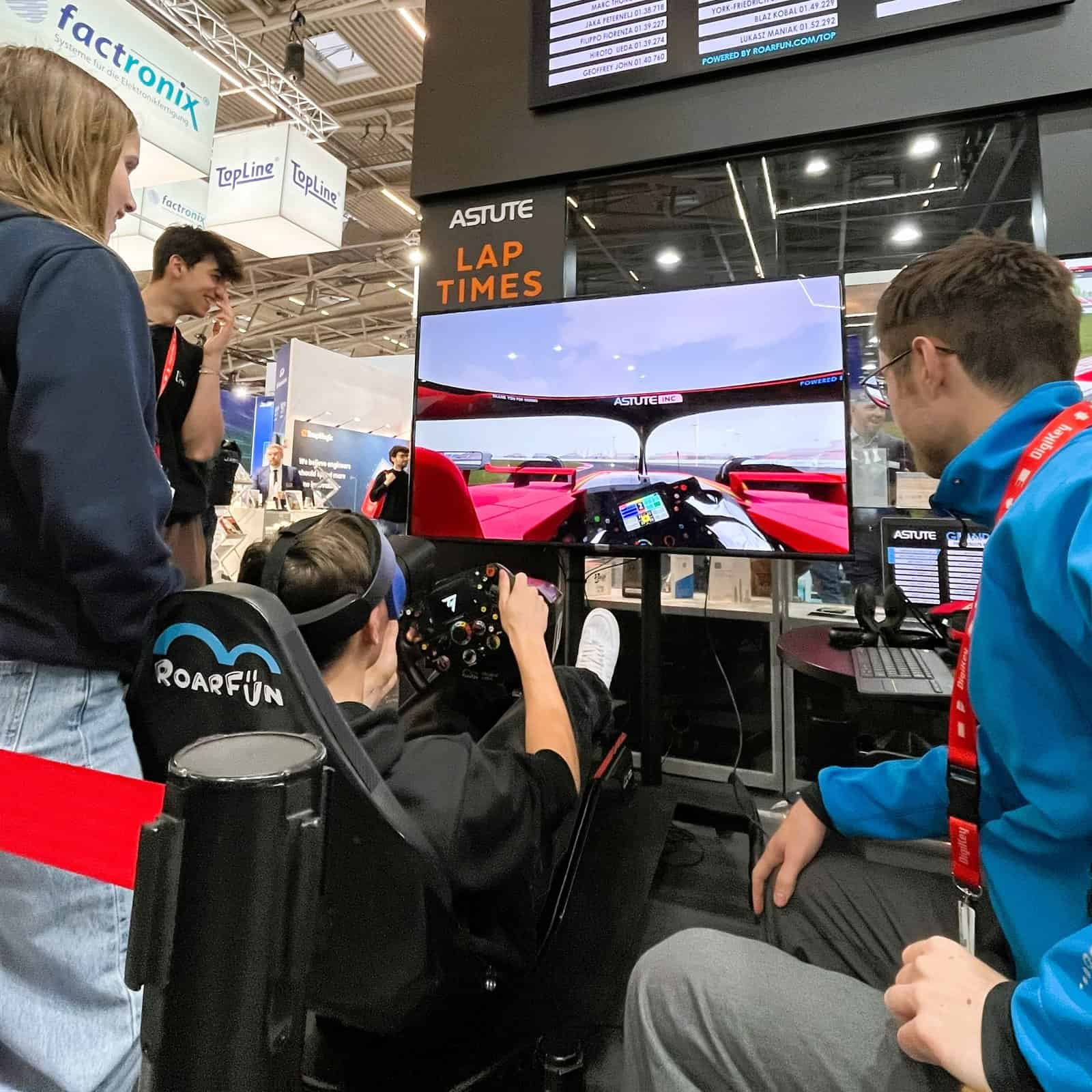 People looking at mobile racing simulator with F1 ferrari steering Wheel.